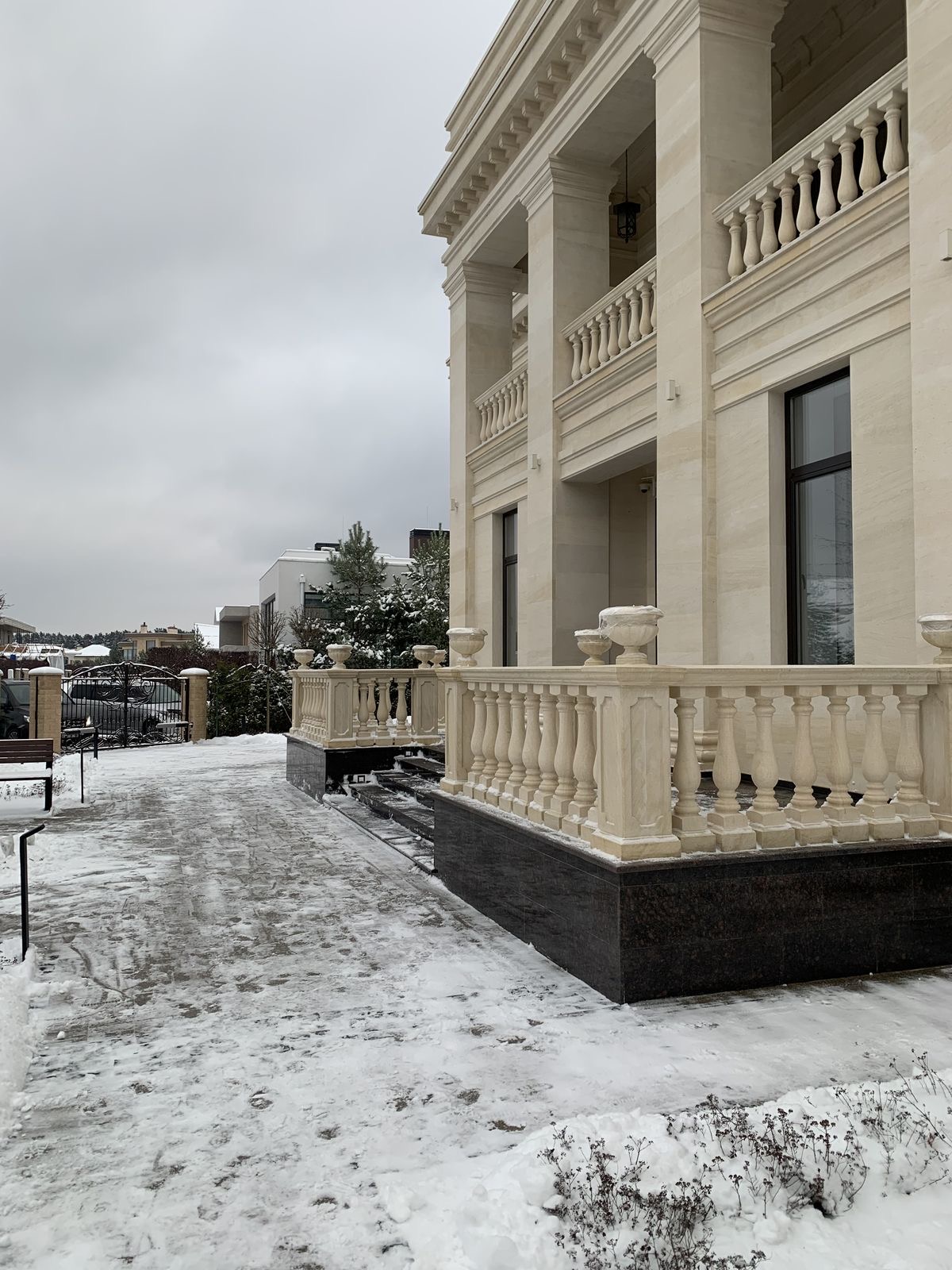 Фасад с колоннами, балясинами и парапетом из светлого камня в зимний период